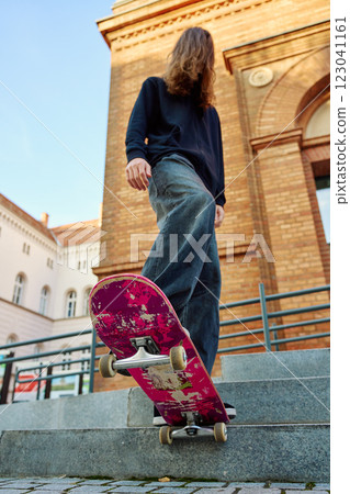 Low angle view of skateboarder balancing on pink skateboard. Close up of underside of deck and wheels of skateboard on stairs at city street 123041161