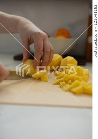 Carefully chop fresh potatoes in a bright and modern kitchen today Carefully chop fresh potatoes in a bright and modern kitchen today 123041162