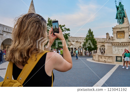 Female tourist with yellow backpack taking photo of historic landmark in Budapest during travel. Woman using smartphone to capture travel and sightseen moments in European city Female tourist with yellow backpack taking photo of historic landmark in Budapest during travel. Woman using smartphone to capture travel and sightseen moments in European city 123041192