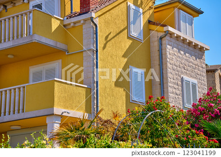 Vibrant yellow villa with white shutters, balcony and lush greenery. Traditional architecture in Croatian village. Rental house for summer vacations in coastal town 123041199