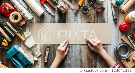A woman uses a craft knife on beige cardstock amidst assorted DIY tools. She's celebrating National DIY Day with a crafting project 123041351