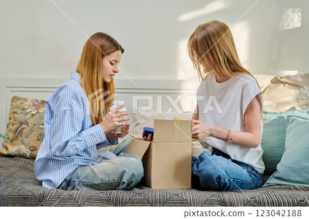 Two young females with cardboard box unpacking an online purchase from internet store 123042188