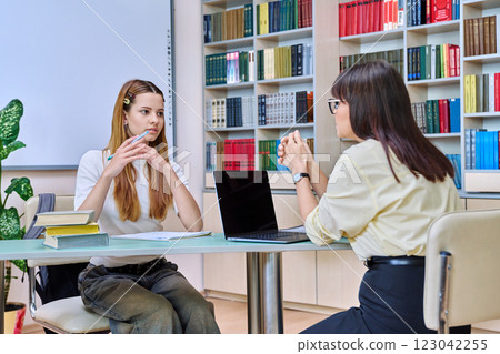 Teenage student girl studies with teacher inside classroom library 123042255