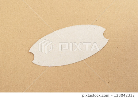 Blank craft paper tag with an oval cutout on textured cardboard. Minimalist label template for branding, handmade product presentation. Diagonal Cardboard cutout label on cardboard background 123042332