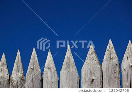 Fence of sharp logs in the form of pencils against the blue sky, close-up Fence of sharp logs in the form of pencils against the blue sky, close-up 123042796