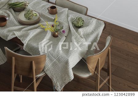Simple organisation of dining table with ceramic dinnerware, linen tablecloth, dining chairs, artichoke and asparagus. Home decoration concept 123042899
