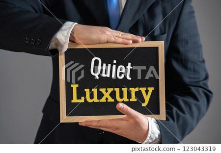 A businessman holds a sign Quiet Luxury. High-end minimalism. Refined wealth, exclusive branding, and premium lifestyle choices. Don't give the appearance of being ultra-rich. Modesty and practicality 123043319