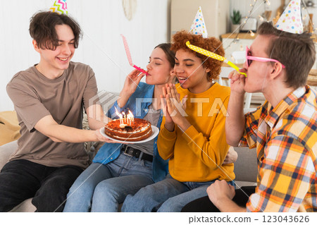 Make a wish. Woman wearing party cap blowing out burning candles on birthday cake. Happy Birthday party. Group of friends wishes girl happy birthday. People celebrating birthday with party at home Make a wish. Woman wearing party cap blowing out burning candles on birthday cake. Happy Birthday party. Group of friends wishes girl happy birthday. People celebrating birthday with party at home 123043626