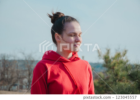 Young woman meditating outdoors in red hoodie on a sunny day Young woman meditating outdoors in red hoodie on a sunny day 123045557