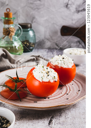Fresh tomatoes filled with cottage cheese and herbs on a plate on the table vertical view Fresh tomatoes filled with cottage cheese and herbs on a plate on the table vertical view 123045619
