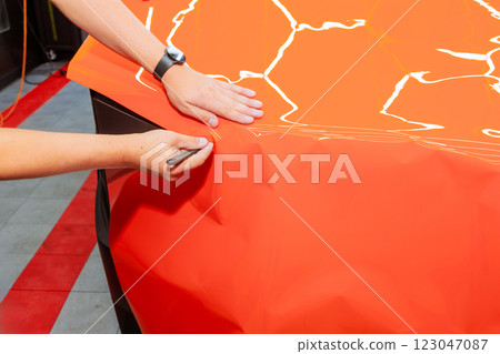 Hands of craftsperson skillfully creating detailed designs on vibrant orange material for protect body automotive in car workshop Hands of craftsperson skillfully creating detailed designs on vibrant orange material for protect body automotive in car workshop 123047087