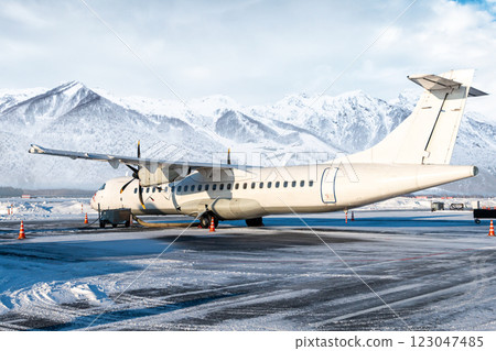 White passenger turboprop airplane on the winter airport on the background of high snow capped mountains White passenger turboprop airplane on the winter airport on the background of high snow capped mountains 123047485