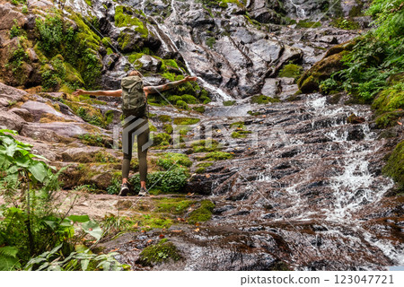 Woman Tourist Standing by Waterfall with Hands Outstretched Woman Tourist Standing by Waterfall with Hands Outstretched 123047721