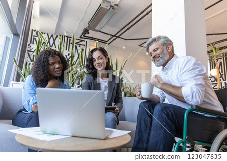 Man in wheelchair collaborating with colleagues in coworking space using laptop and internet Man in wheelchair collaborating with colleagues in coworking space using laptop and internet 123047835