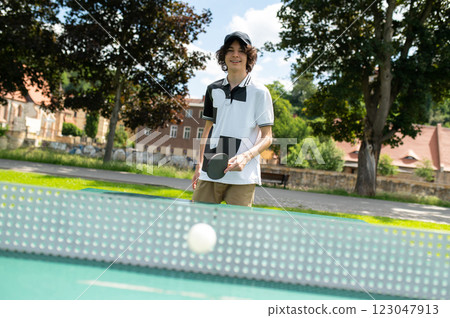 Caucasian young guy in black cap playing table tennis and feeling excited 123047913