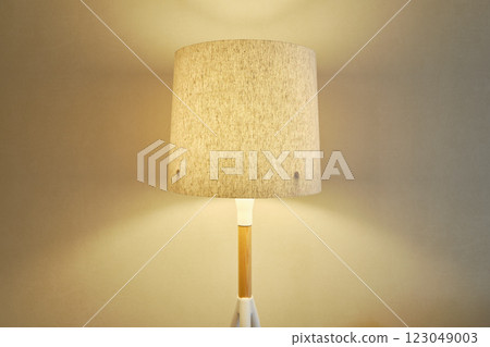 A stylish lamp with a beige fabric shade casting a soft warm light on the wall A stylish lamp with a beige fabric shade casting a soft warm light on the wall 123049003