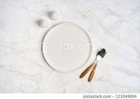 Minimalist dining setup featuring an empty plate and utensils on a marble table Minimalist dining setup featuring an empty plate and utensils on a marble table 123049004