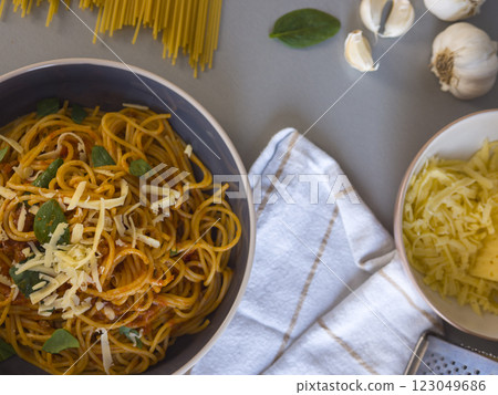 Balanesi pasta in a bowl, topped with grated cheese and fresh basil, surrounded by raw spaghetti, garlic cloves, and additional cheese, creating a vibrant culinary scene Balanesi pasta in a bowl, topped with grated cheese and fresh basil, surrounded by raw spaghetti, garlic cloves, and additional cheese, creating a vibrant culinary scene 123049686