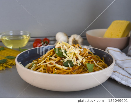 Balanesi pasta with tomato sauce. Grated cheese and basil leaves served in a modern bowl. With raw pasta. Cherry tomatoes. Garlic. Olive oil and grated cheese in the background 123049691