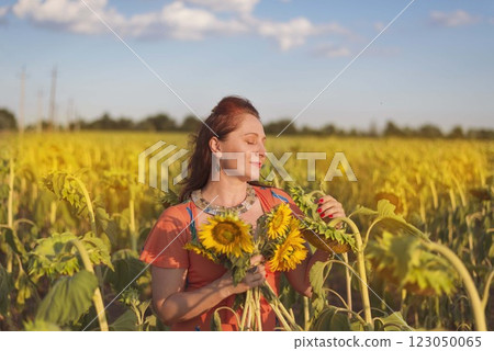 a woman of 35-40 years old stands in a field where large sunflowers grow. a woman of 35-40 years old stands in a field where large sunflowers grow. 123050065
