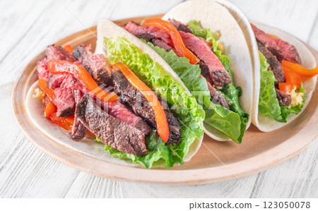 Three carne asada tacos filled with steak, grilled peppers, lettuce, and cheese 123050078