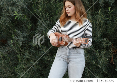 Girl Strums With Ukulele Musical Instrument Near A Tree In The Mountains 123050229