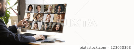 Business professional pointing at screen, leading online discussion with diverse virtual team displayed on monitor against minimalist office. 123050398