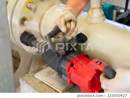 Worker using an electric impact wrench to dismantle a pipeline flange connection. 123050427