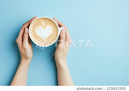 Woman holding cup of cappuccino with heart shape latte art on blue background 123051505