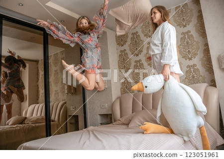 Women Bedroom Fun Pillow Joyful friends playfully jump, pose with large plush bird, modern bedroom. 123051961