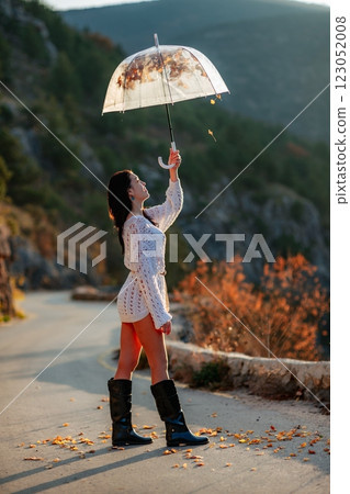 woman umbrella leaves , She holds him over her head, autumn leaves are falling out of him. Beautiful woman in a dress with an umbrella in the autumn park on the road in the mountains. 123052008