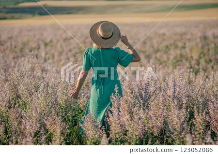 Woman Dress Field: Summer, Lavender Field, Relaxed Stroll. A woman in a teal dress walks through a lavender field during a sunny summer day, enjoying the scenery. 123052086