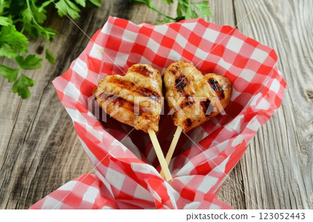 Two grilled heart shaped kebabs wrapped in checkered paper resting on rustic wooden table 123052443