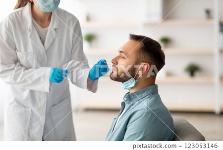Covid diagnostic procedure. Doctor making nasal PCR test for young Caucasian man, using sterile swab stick at home. Millennial guy undergoing coronavirus analysis, checking health 123053146
