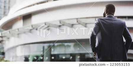 Rear view of unrecognizable confident black businessman in suit with his hands in pockets against modern office center background, copy space 123053153
