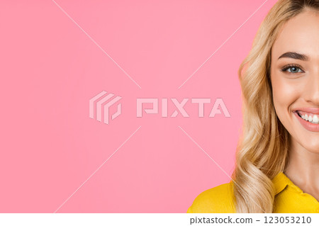 This image features a close-up of a young woman with blonde hair smiling against a pink background. Her right side is shown, with only her eye, cheek, and smile visible, copy space 123053210