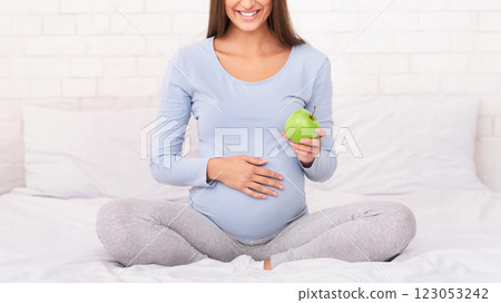 Pregnancy Nutrition. Unrecognizable Pregnant Lady Holding Apple Sitting On Bed In Bedroom. Cropped 123053242