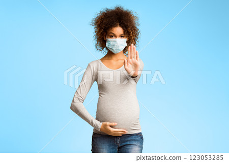 Afro pregnant woman in medical face mask gesturing stop over gray studio background 123053285