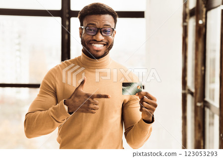 Cashback Concept. Happy black businessman pointing at plastic credit card, recommending it. Copy space 123053293