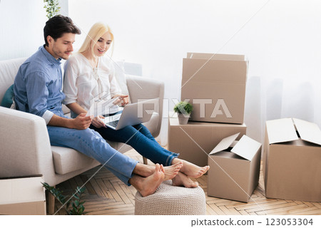 Buying House. Cheerful Couple Using Laptop Looking Through Ownership Papers Sitting On Sofa After Moving Apartment. Free Space 123053304