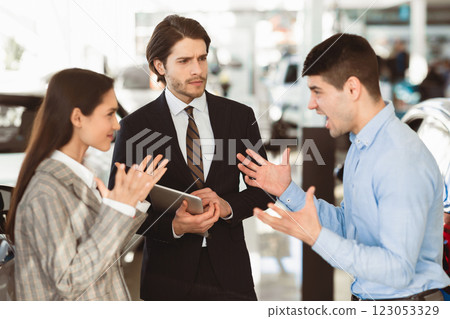 Car Seller Looking At Couple Having Quarrel About Buying Too Expensive Car In Dealership Showroom. Selective Focus Car Seller Looking At Couple Having Quarrel About Buying Too Expensive Car In Dealership Showroom. Selective Focus 123053329
