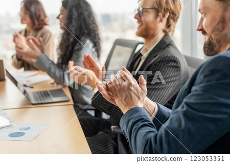A group of business professionals are seated around a conference table, clapping their hands in appreciation. A laptop and papers are visible on the table. A group of business professionals are seated around a conference table, clapping their hands in appreciation. A laptop and papers are visible on the table. 123053351