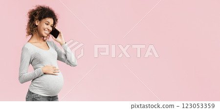 African-american expectant woman having phone conversation and touching belly over pink studio background 123053359