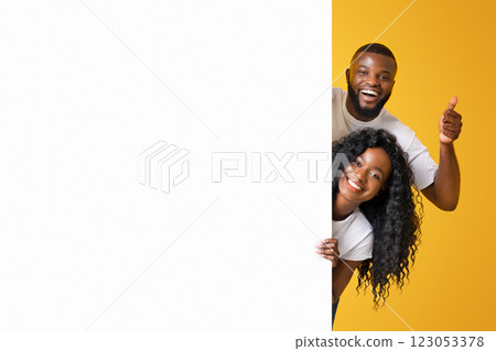A couple smiles and gives a thumbs up as they peek around a corner against a bright yellow background. A couple smiles and gives a thumbs up as they peek around a corner against a bright yellow background. 123053378