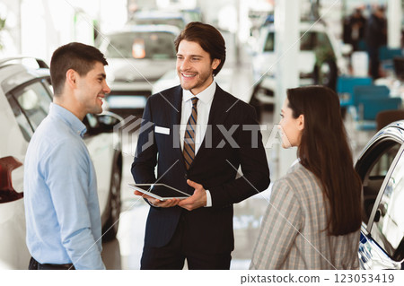 Discussing The Purchase. Young Family Speaking With Professional Car Seller In Dealership Center Discussing The Purchase. Young Family Speaking With Professional Car Seller In Dealership Center 123053419