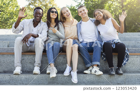Happy friends international students spending time together in the summer city, sitting on stairs and smiling Happy friends international students spending time together in the summer city, sitting on stairs and smiling 123053420