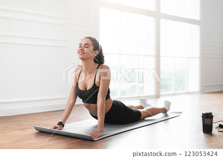 Relief Lower Back Pain. Smiling Young Woman Doing Sphinx Cobra Pose Or Upward-Facing Dog Asana Stretching Back Muscles Practicing Pilates, Excercising At Fitness Studio Or In Living Room On Yoga Mat 123053424