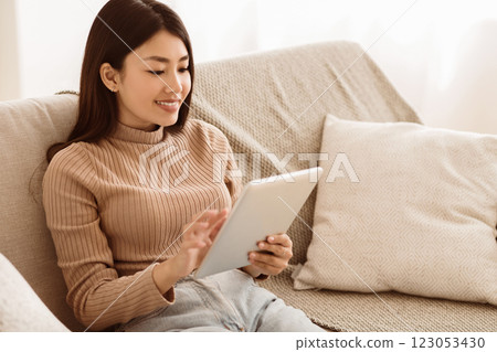 Teen Girl Watching Media Content on Tablet, Sitting on Sofa at Home, Copy Space 123053430