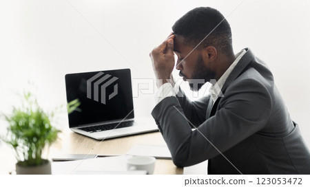 A businessman sits at a desk, his head in his hands, looking stressed. A businessman sits at a desk, his head in his hands, looking stressed. 123053472