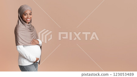 Expecting baby. Portrait of pregnant afro muslim woman in headscarf embracing her belly, posing over yellow background in studio, copy space Expecting baby. Portrait of pregnant afro muslim woman in headscarf embracing her belly, posing over yellow background in studio, copy space 123053489